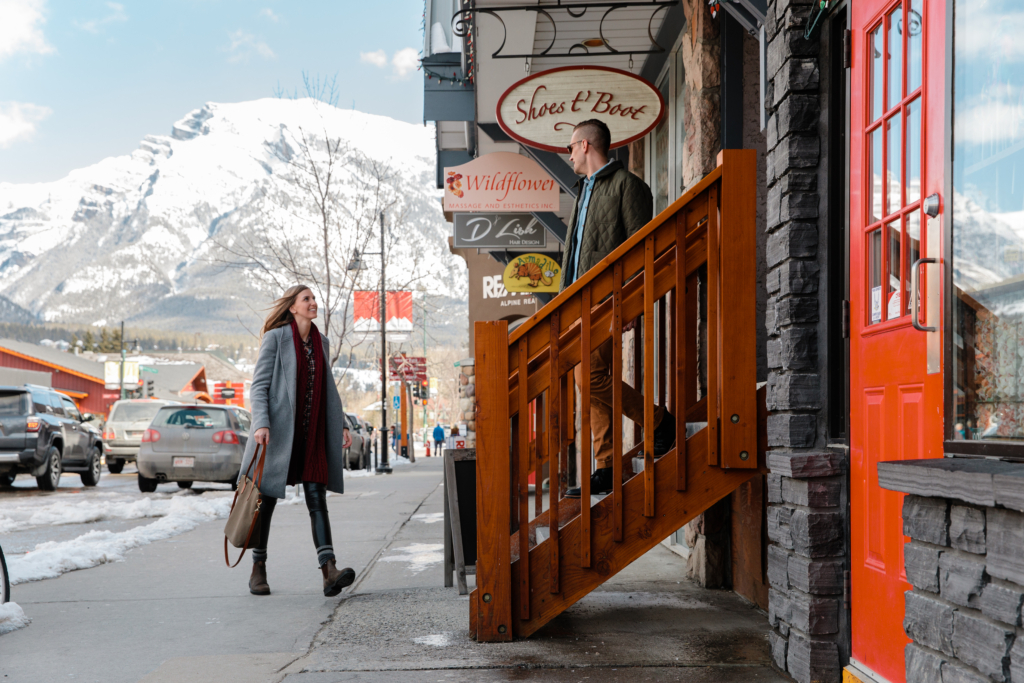 Man and woman shopping in downtown Canmore, strolling streets with snowy mountain peaks in the background.