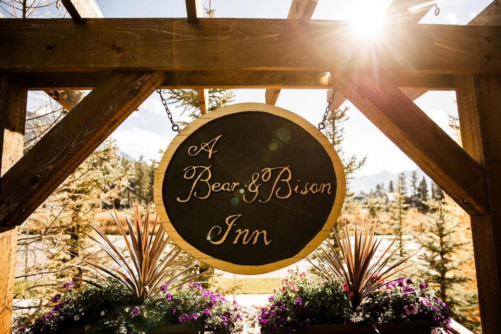 Wooden sign for A Bear and Bison Inn framed by golden larch trees in Canmore.